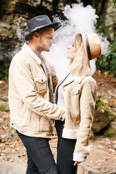 Couple in vape cloud. Two in smoke. Tourists in cold autumn forest with vape. Man and women in smoke. Two smokers. Beautiful couple in fog. E-cigarettes and people.
