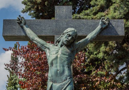 A statue of Jesus Christ crucified against some trees. Jesus Christ on cross. Jesus christ statue in the cemetery.