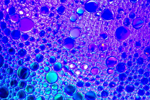 Colorful drops of oil on the water. Blue and violet colored circles and ovals. Abstract bright background for design.