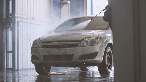 Woman worker with the water hose in car-washing facility
