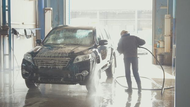 Woman worker with the water hose in car-washing facility