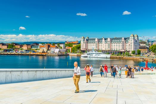 Oslo - June 2019, Norway: Beautiful cityscape of Oslo on a summer day. A group of tourists climbing up to the observation point on top of the Opera House