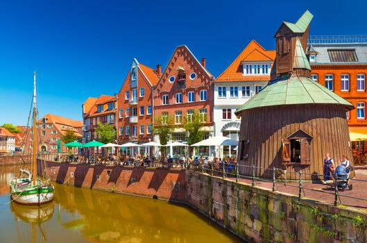 Stade - July 2019, Germany: View of a small German town with the traditional architecture, promenade with walking people and canal with an old wooden ship