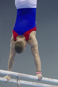 Rear view of muscular man gymnasts competing on the bar