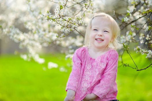 Adorable toddler girl in blooming cherry garden