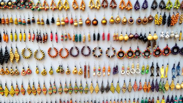 Concept: the value of craftsmanship. Many handmade colored wooden earrings displayed in a row for sale