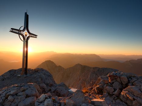 Cross raised  at mountain summit  in Alps. Sharp peak, daybreak Sun