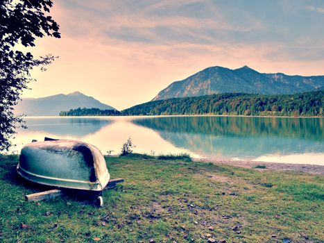 Upside down  fishing paddle boat on bank of Alps lake. Morning autumnal lake.