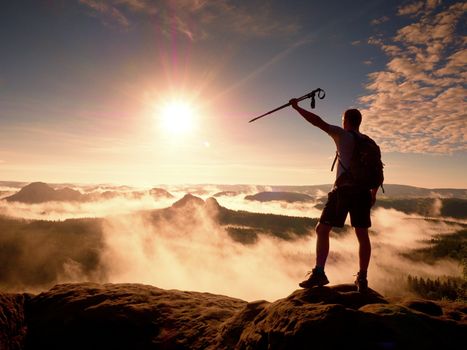 Tall backpacker with poles in hand. Sunny misty daybreak in rocky mountains.