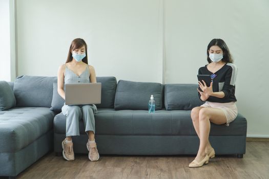 Coronavirus or COVID-19 is spreading. Two Asian women wearing medical masks Keep the distance Are using laptops and tablets at home .social distancing is a new normal life