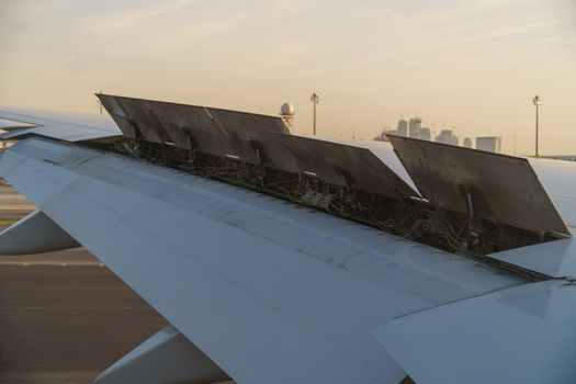 View from the passenger window - Wing of an airplane landing above the runway at high speed during the sunset with flaps raised