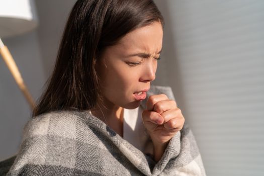 Asian woman coughing in fist sick of coronavirus viral infection spreading corona virus by not covering mouth and nose. Painful cough ill young chinese girl at home
