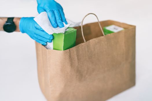 Disinfection of food home delivery sanitizing packages of online shopping bag with disinfecting wipes. Sanitizing surfaces of packages on groceries with gloves. COVID-19 precaution hygiene