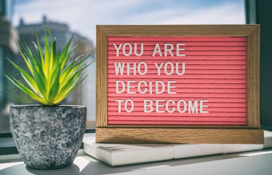 Inspiration quote message sign saying You are who you decide to become - life advice for self esteem, confidence. Home background