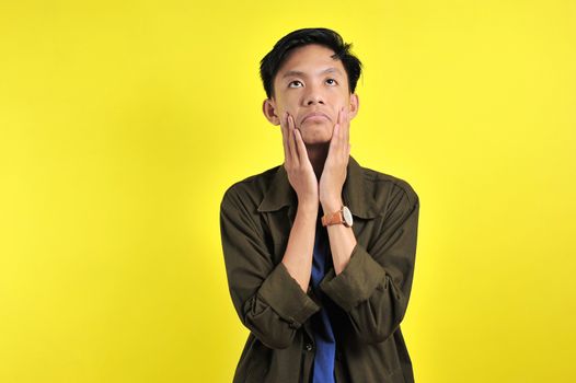 Confused man doing foolish gesture, disappointed expression, isolated on yellow background