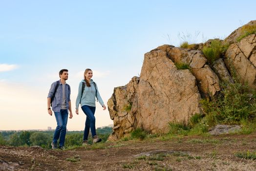 Young Happy Travelers Hiking with Backpacks on the Rocky Trail at Summer Sunset. Family Travel and Adventure Concept.