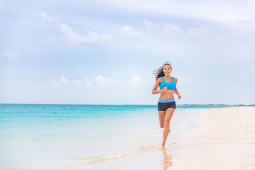 Exercise fitness athlete woman jogging on beach training cardio in summer vacation background. Blue ocean water, sun sky landscape. Happy Asian girl running barefoot outside