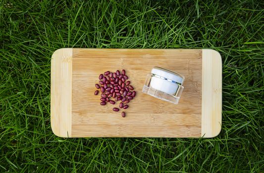 red kidney beans beside a beauty cream container on top of a wood cutting board, laying on top of green grass