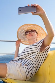 Beautiful, romantic blonde woman taking selfie self portrait photo on summer vacations traveling by cruse ship ferry boat.