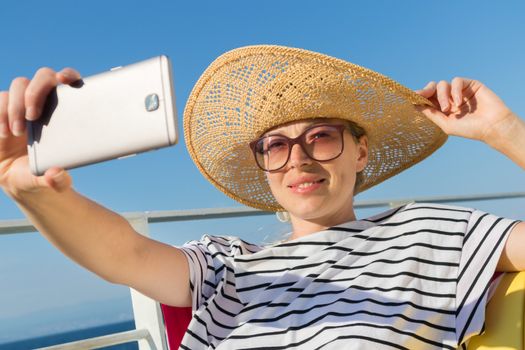 Beautiful, romantic blonde woman taking selfie self portrait photo on summer vacations traveling by cruse ship ferry boat.