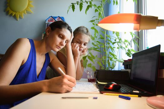Mother solves daughter's assignments to study in notebooks at home at the desk