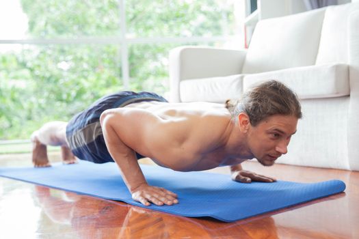 Close up of young man doing push up exercise on mat in living ro