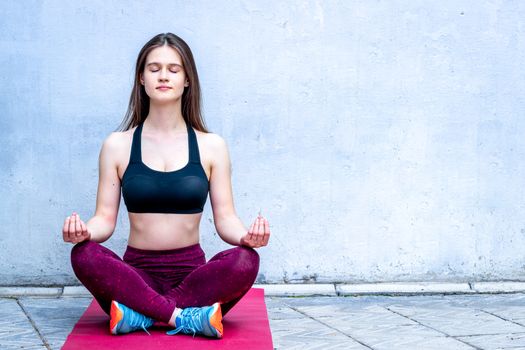 Meditation. Girl in sport wear relax in yoga asana - blue wall, copy space.
