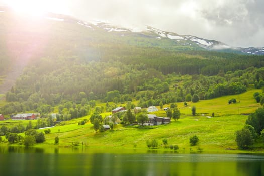 Village is located on the green slopes near lake. Scenic summer view of cottage houses in mountain village near lake, Norway. Tourism holidays and travel.