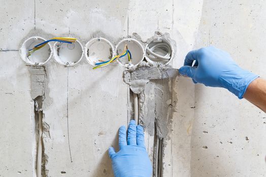 hidden installation of electrical wires for sockets to a concrete wall. The master is plastering the strobes with the wire before the molar works. repair in an old apartment and transfer of sockets.