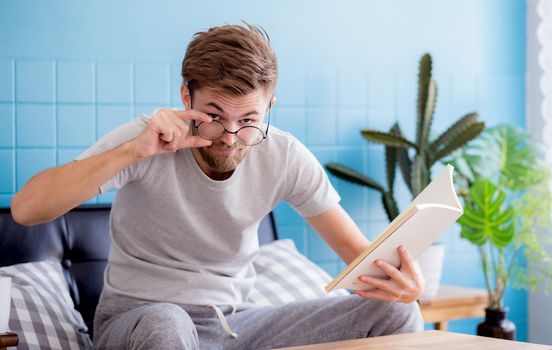 Young man wear glasses reading book on sofa in the living rooman