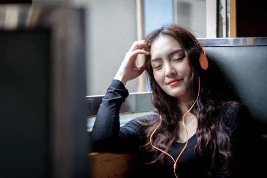 Asian woman traveler has listening music with phone and orange headphone inside the train at Hua Lamphong station at Bangkok, Thailand.