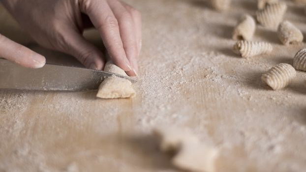 Close up process of homemade vegan gnocchi pasta with wholemeal flour making. The home cook cuts the dough on the wooden chopping board , traditional Italian pasta, woman cooks food in the kitchen