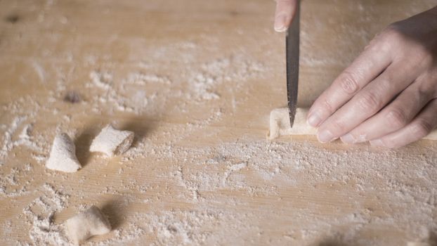 Close up process of homemade vegan gnocchi pasta with wholemeal flour making. The home cook cuts the dough on the wooden chopping board , traditional Italian pasta, woman cooks food in the kitchen