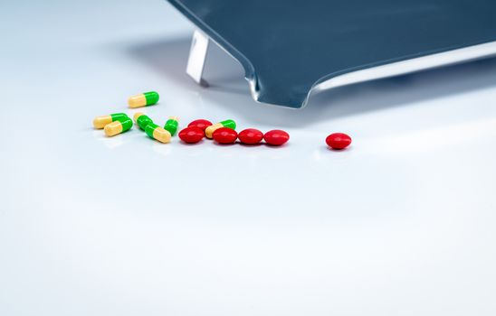 Red tablets and green-yellow capsules pills with drug tray on wh
