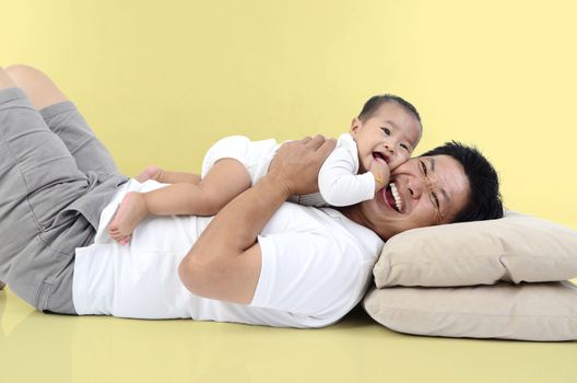 Happy father's day! joyful young dad  hugging his cute son and lying on floor at home. Isolated on yellow background.
