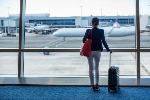 Businesswoman traveling in airport. Woman looking through the window at tarmac and planes waiting for flight. Business travel concept