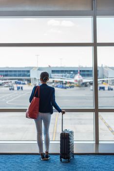 Silhouette of woman waiting at airport terminal for flight boarding. Businesswoman traveling looking through the window at tarmac and planes. Business travel concept