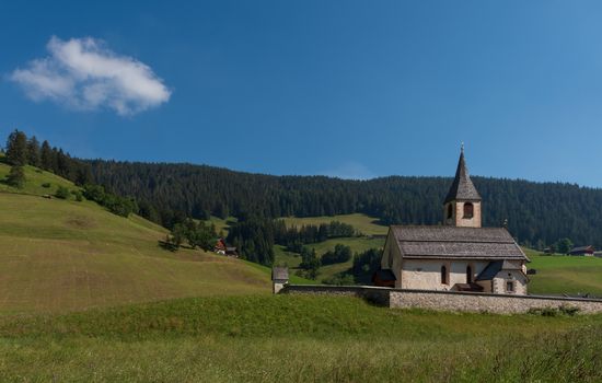 South Tyrolean mountain church under a blue sky with a single wh