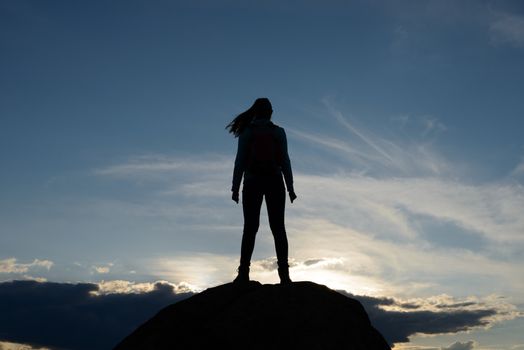 Young Woman Traveler with Backpack Standing on the Top of the Rock at Summer Sunset. Travel and Adventure Concept.