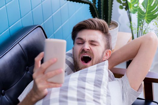 american man watching media content in a smart phone and yawn on