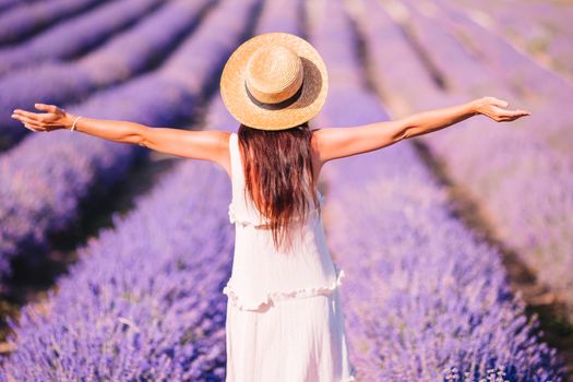 Woman in lavender flowers field at sunset in white dress and hat