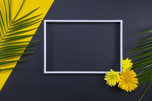 Frame of tropical palm leaves and flowers on black and yellow background. Flat lay, top view, copy space. Summer background, nature. Creative frame background with tropical leaves.