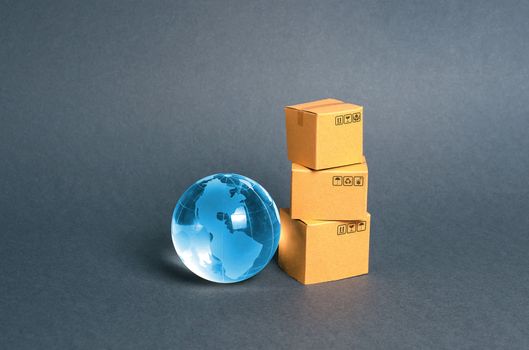 Blue glass planet globe and a stack of cardboard boxes. The concept of commerce and trade, cargo delivery, exchange of goods. Globalization, markets. Business and industry, transport infrastructure.