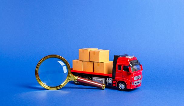 Red truck loaded with boxes and a magnifying glass. Search for a carrier and routes for transportation. Tracking freight. Transit of goods and products. Customs inspection and fees payment. Business