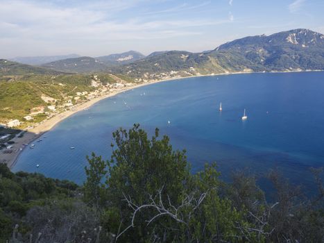 Panoramic view of Agios Georgios Pagon sand beach with green hills and sailing ships at Corfu island, Greece, sunny day blue sky