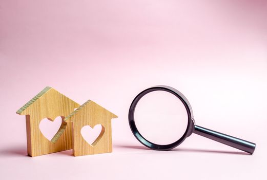 Two wooden house with a heart and a magnifying glass. The concept of finding affordable housing for young families and married couples. Mortgage. Rent a home for a romantic holiday on Valentine's Day.