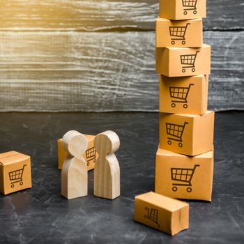 Two wooden people stand near a tower of boxes. buyer and seller, manufacturer and retailer. Business and commerce. Discussion of the terms of the trading deal, the purchase of goods and services.