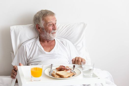 Senior retirement male has breakfast with orange juice and water on bed