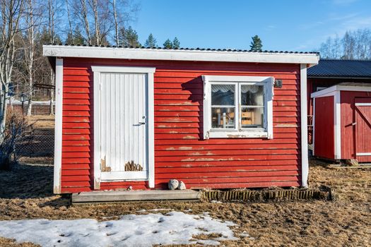 Typical small red colored guest house with one white door and white window at Swedish country side needs immediate renovation - old paint flake off, some boards are rotten
