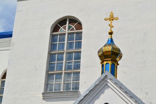 Golden dome of the Orthodox church in Belarus. Byzantine cross with window and white wall